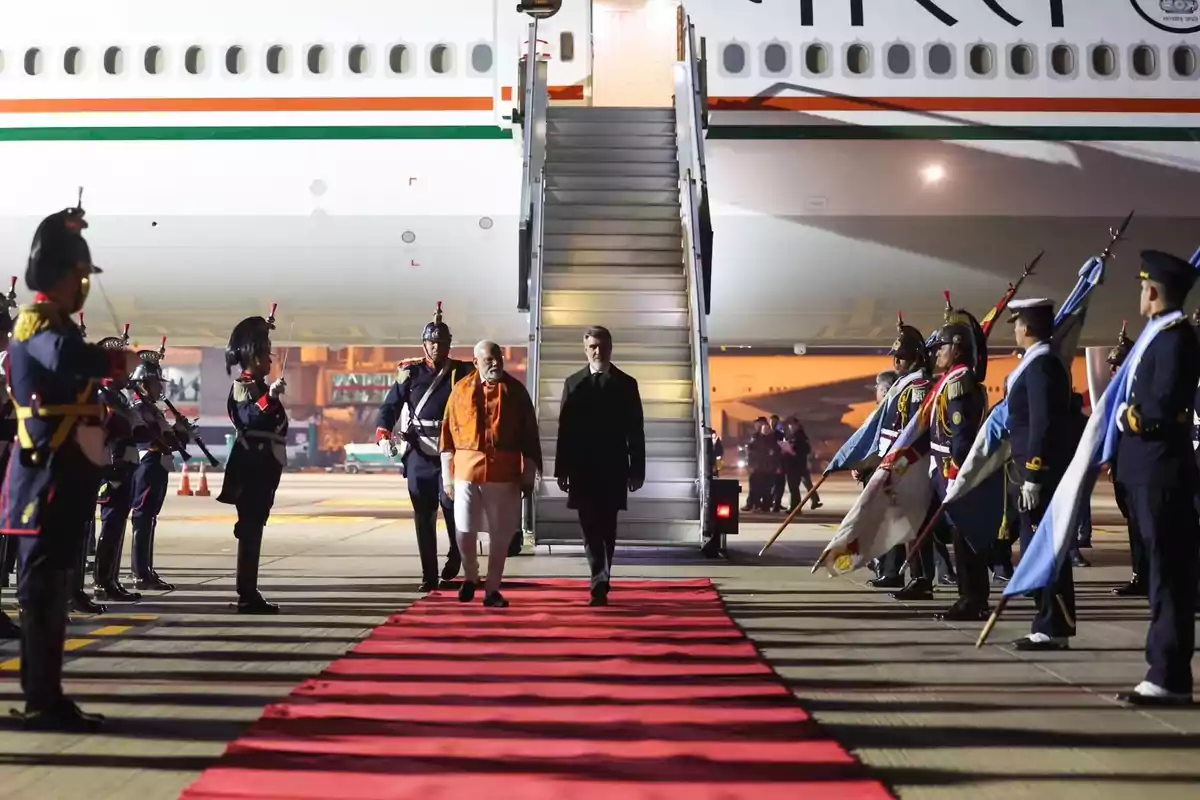 Two people get off a plane and walk on a red carpet while being received with military honors by a uniformed guard. Two people get off a plane and walk on a red carpet while being received with military honors by a uniformed guard.