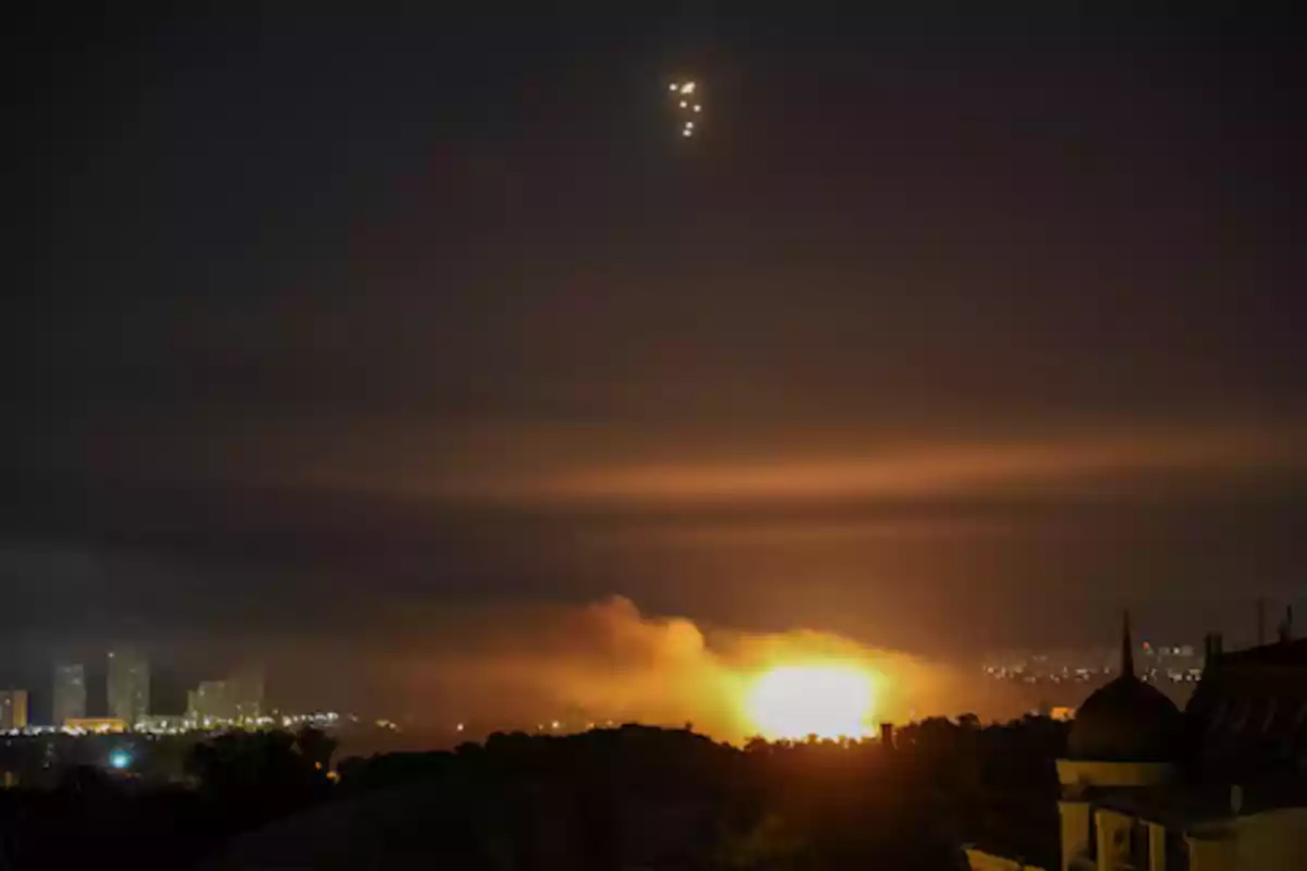 Explosión iluminando el cielo nocturno en una ciudad con destellos brillantes en el aire y edificios al fondo Explosión iluminando el cielo nocturno en una ciudad con destellos brillantes en el aire y edificios al fondo