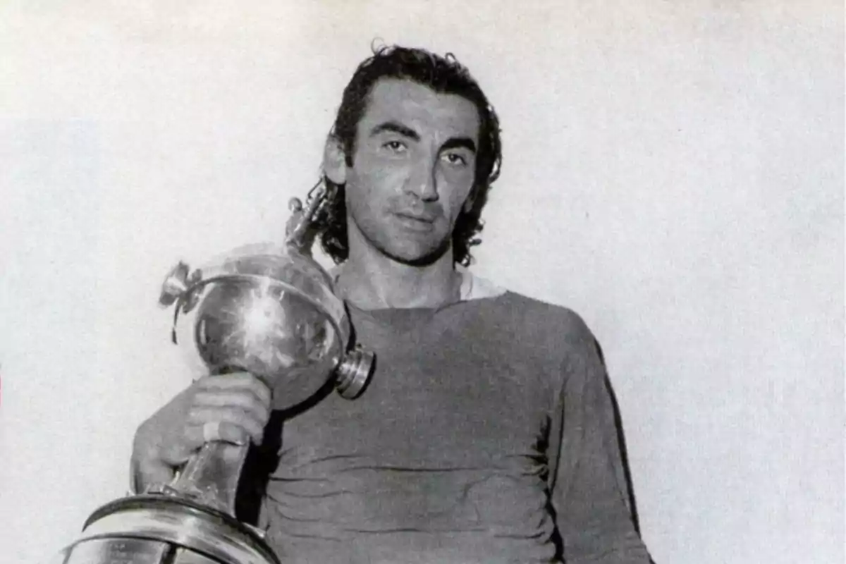 Soccer player holding a large trophy with a serious expression in a black and white photograph Soccer player holding a large trophy with a serious expression in a black and white photograph