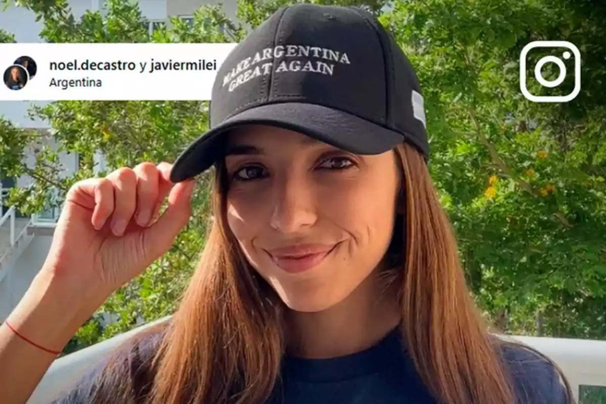 Mujer joven con cabello largo y lacio usando una gorra negra que dice Make Argentina Great Again, sonriendo y posando al aire libre con árboles de fondo