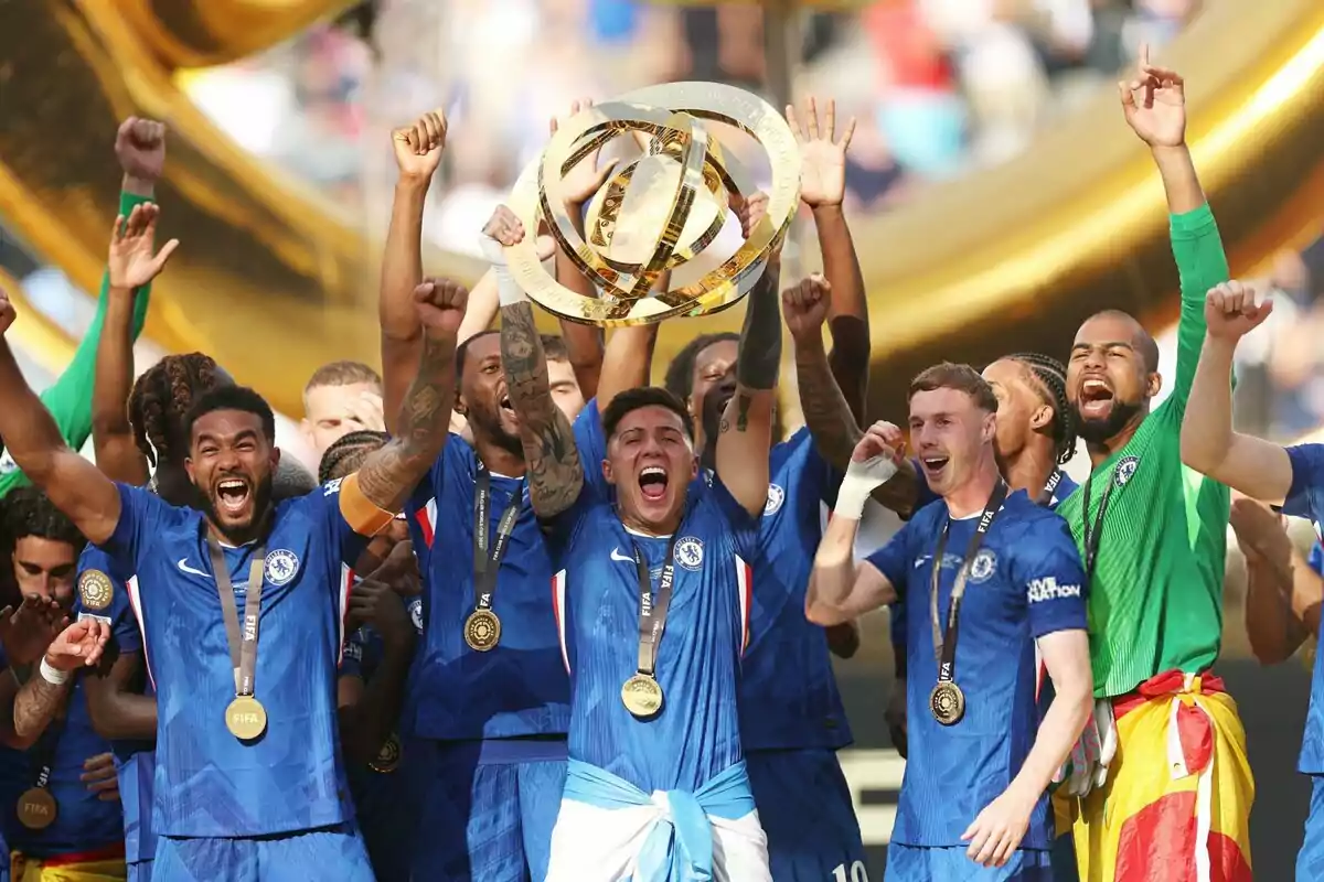 Jugadores de un equipo de fútbol celebran eufóricos levantando un trofeo dorado mientras usan medallas y visten uniformes azules Jugadores de un equipo de fútbol celebran eufóricos levantando un trofeo dorado mientras usan medallas y visten uniformes azules