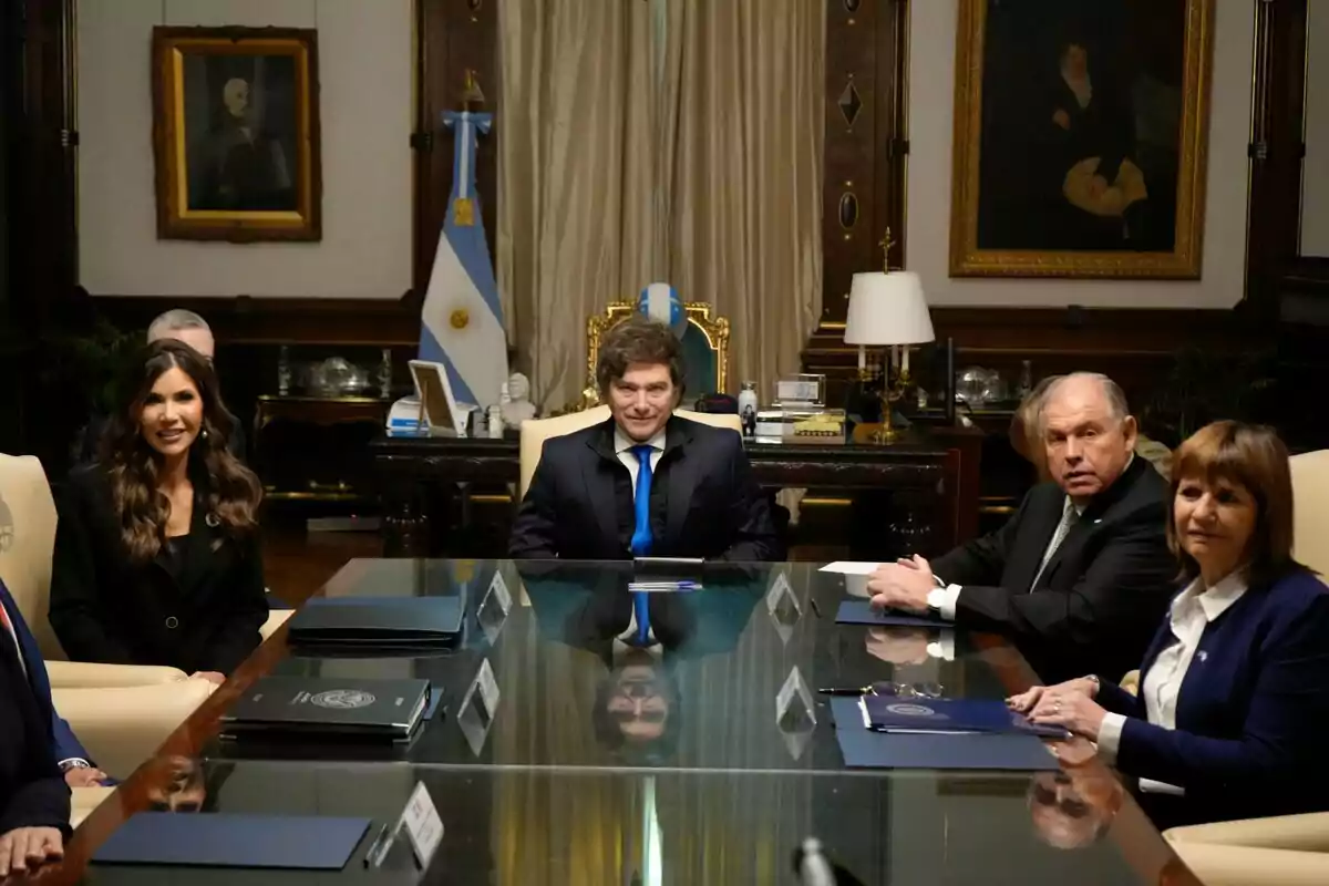 Un grupo de personas sentadas alrededor de una mesa de reuniones en una oficina elegante con banderas argentinas y cuadros en las paredes
