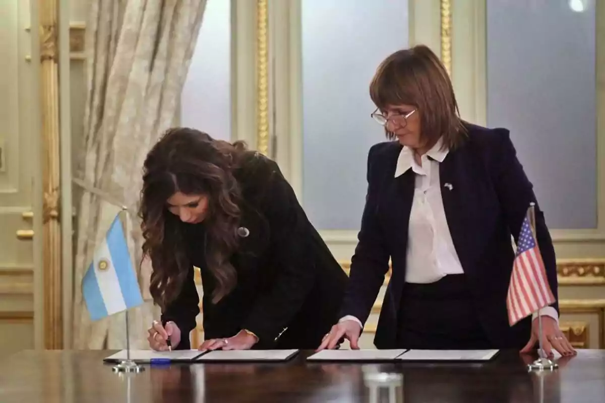 Dos mujeres firmando documentos en una mesa con banderas de Argentina y Estados Unidos en un entorno formal Dos mujeres firmando documentos en una mesa con banderas de Argentina y Estados Unidos en un entorno formal