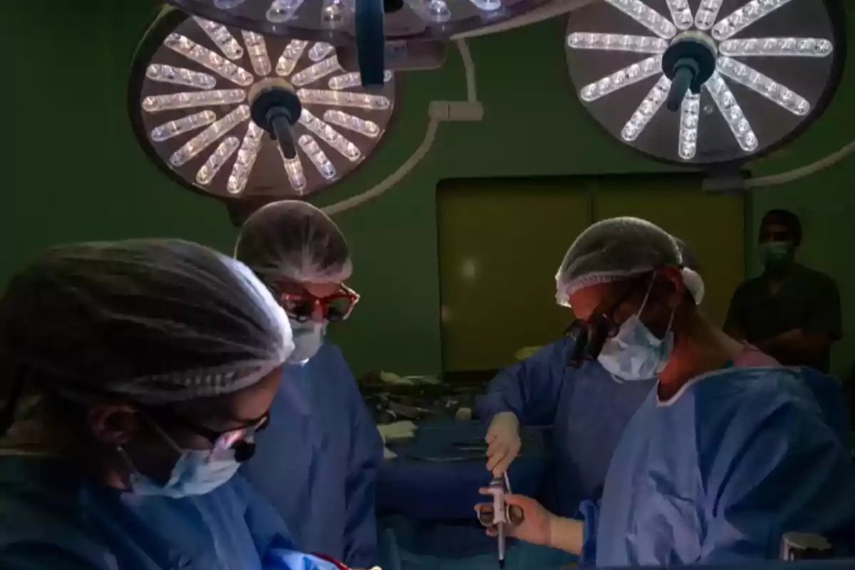 Equipo de cirujanos realizando una operación en una sala de quirófano iluminada con lámparas quirúrgicas Equipo de cirujanos realizando una operación en una sala de quirófano iluminada con lámparas quirúrgicas