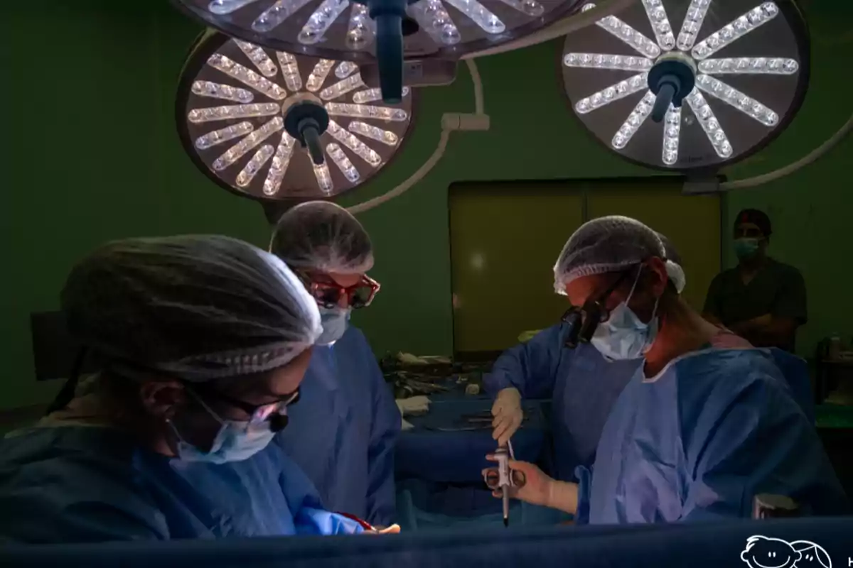 Equipo de cirujanos realizando una operación en un quirófano iluminado con lámparas quirúrgicas mientras usan mascarillas y gorros de protección