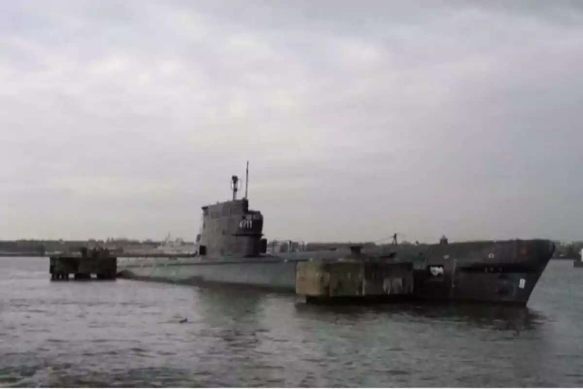 Gray military submarine docked next to a pier on a cloudy day Gray military submarine docked next to a pier on a cloudy day