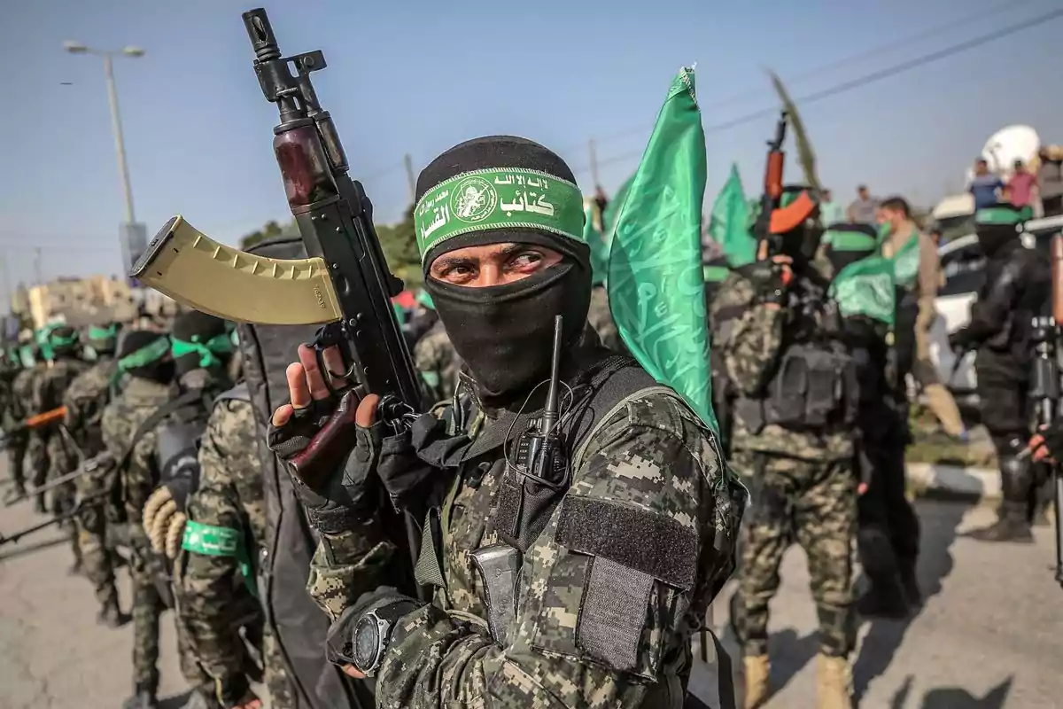 Grupo de hombres armados con uniformes de camuflaje y pañuelos verdes en la cabeza reunidos en una calle