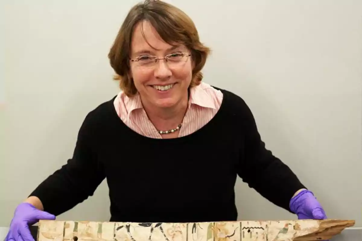Smiling woman with glasses and purple gloves holds an ancient object decorated with Egyptian hieroglyphs Smiling woman with glasses and purple gloves holds an ancient object decorated with Egyptian hieroglyphs