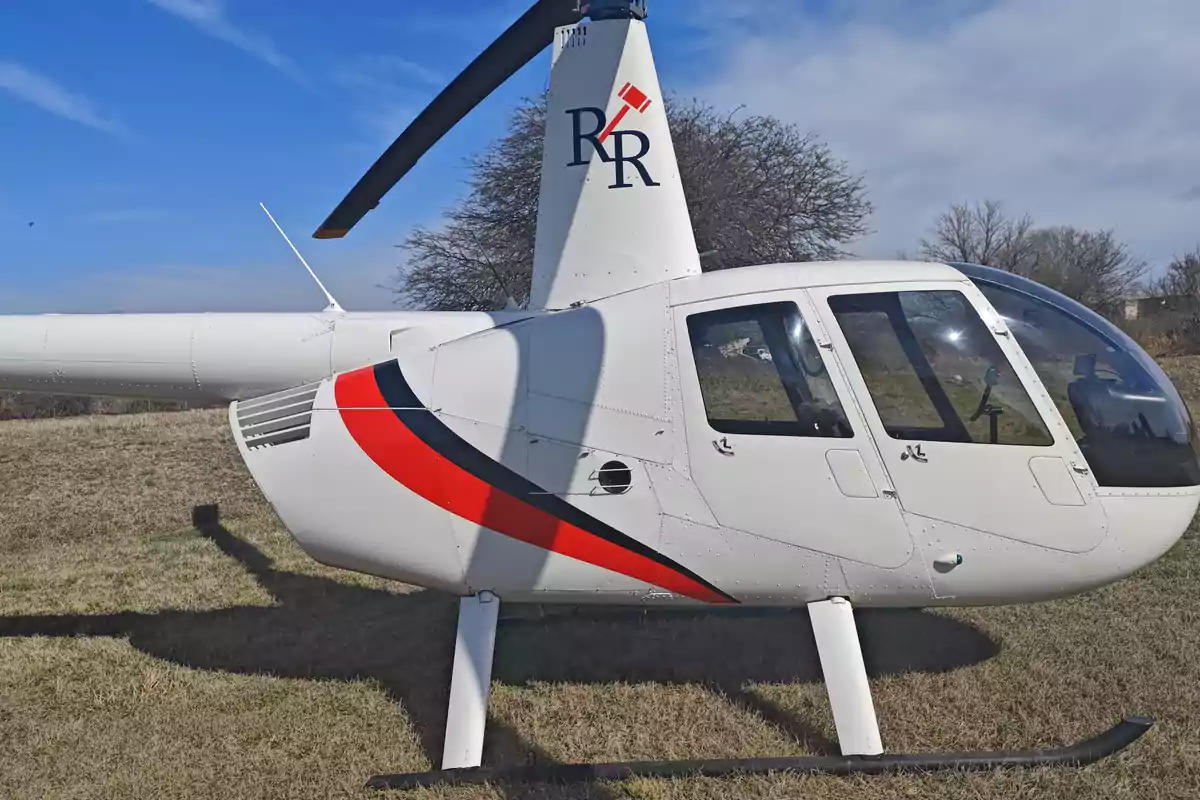 Helicóptero blanco con detalles en rojo y negro estacionado sobre césped bajo un cielo azul