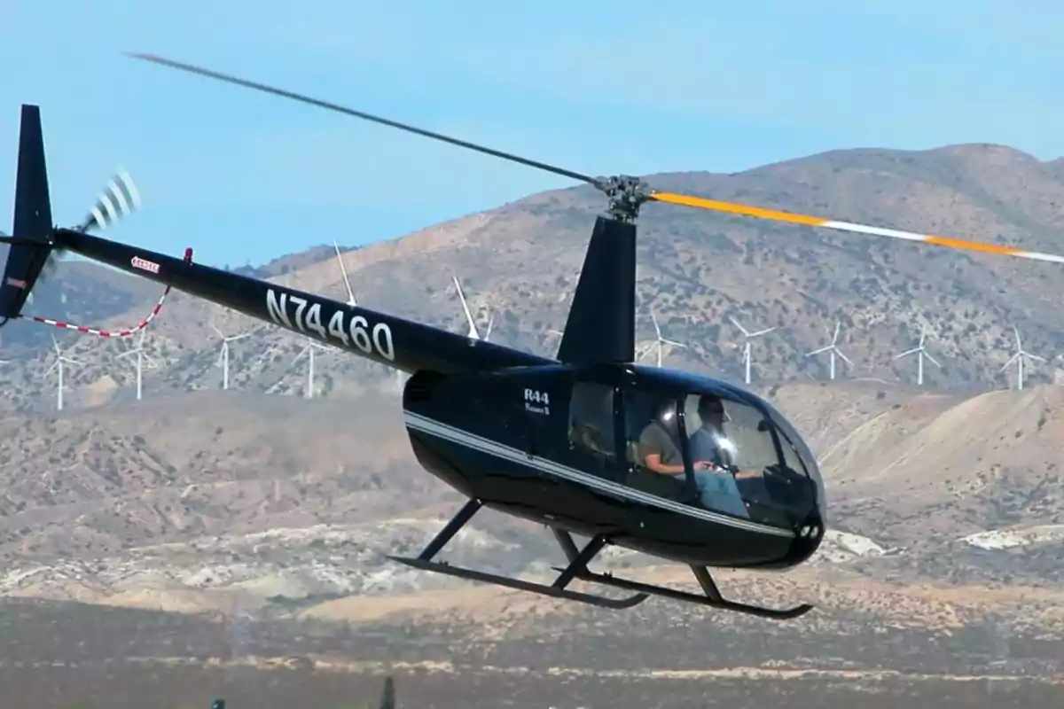 Helicóptero negro volando sobre un paisaje montañoso con aerogeneradores al fondo Helicóptero negro volando sobre un paisaje montañoso con aerogeneradores al fondo