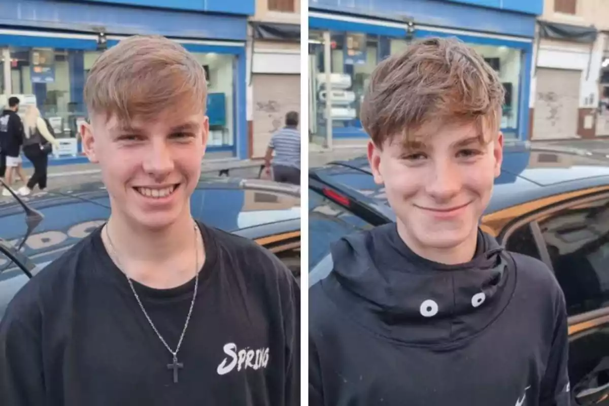 Two teenagers smile in front of a black car on an urban street with shops in the background.