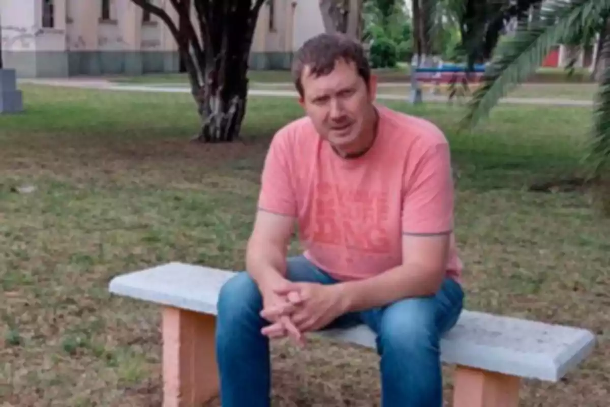 Man sitting on a concrete bench in a park with grass and trees in the background Man sitting on a concrete bench in a park with grass and trees in the background
