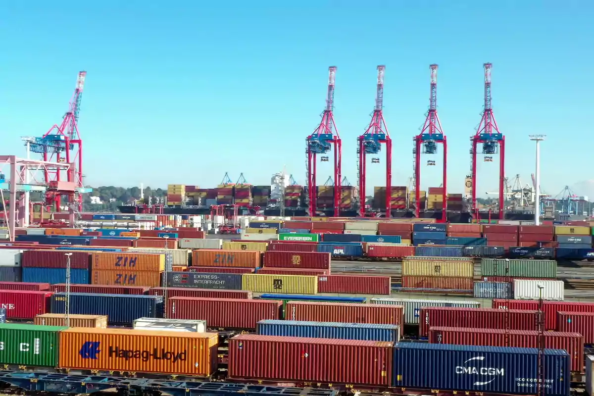 Vista de un puerto con grúas rojas y numerosos contenedores de carga apilados en diferentes colores