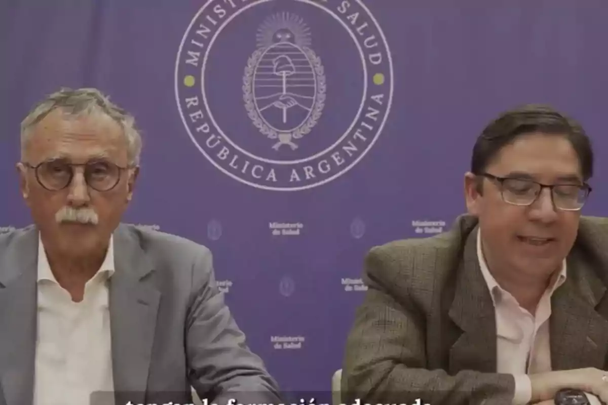 Dos hombres con gafas sentados frente a un fondo violeta con el logo del Ministerio de Salud de la República Argentina Dos hombres con gafas sentados frente a un fondo violeta con el logo del Ministerio de Salud de la República Argentina