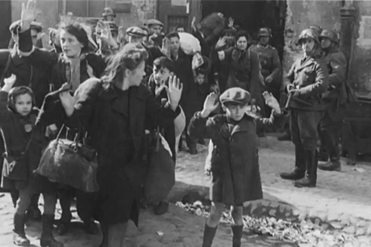 Grupo de personas con las manos en alto siendo escoltadas por soldados en una calle durante la Segunda Guerra Mundial