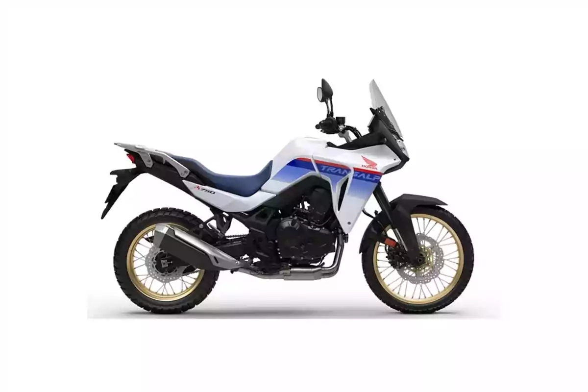 Motocicleta tipo trail de color blanco con detalles en azul y rojo, llantas de rines dorados y diseño robusto para aventura Motocicleta tipo trail de color blanco con detalles en azul y rojo, llantas de rines dorados y diseño robusto para aventura