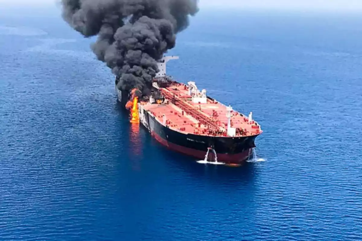 An oil tanker at sea is on fire and is emitting a large column of black smoke. An oil tanker at sea is on fire and is emitting a large column of black smoke.