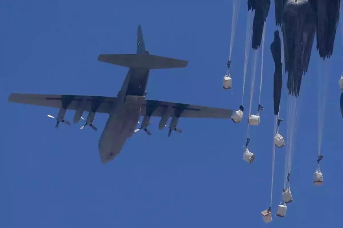 Military plane seen from below dropping supplies with parachutes in the clear sky Military plane seen from below dropping supplies with parachutes in the clear sky