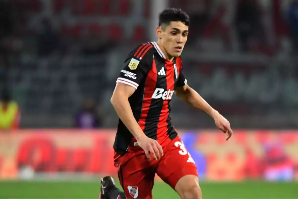 Jugador de fútbol con uniforme negro y rojo de River Plate corriendo en la cancha durante un partido