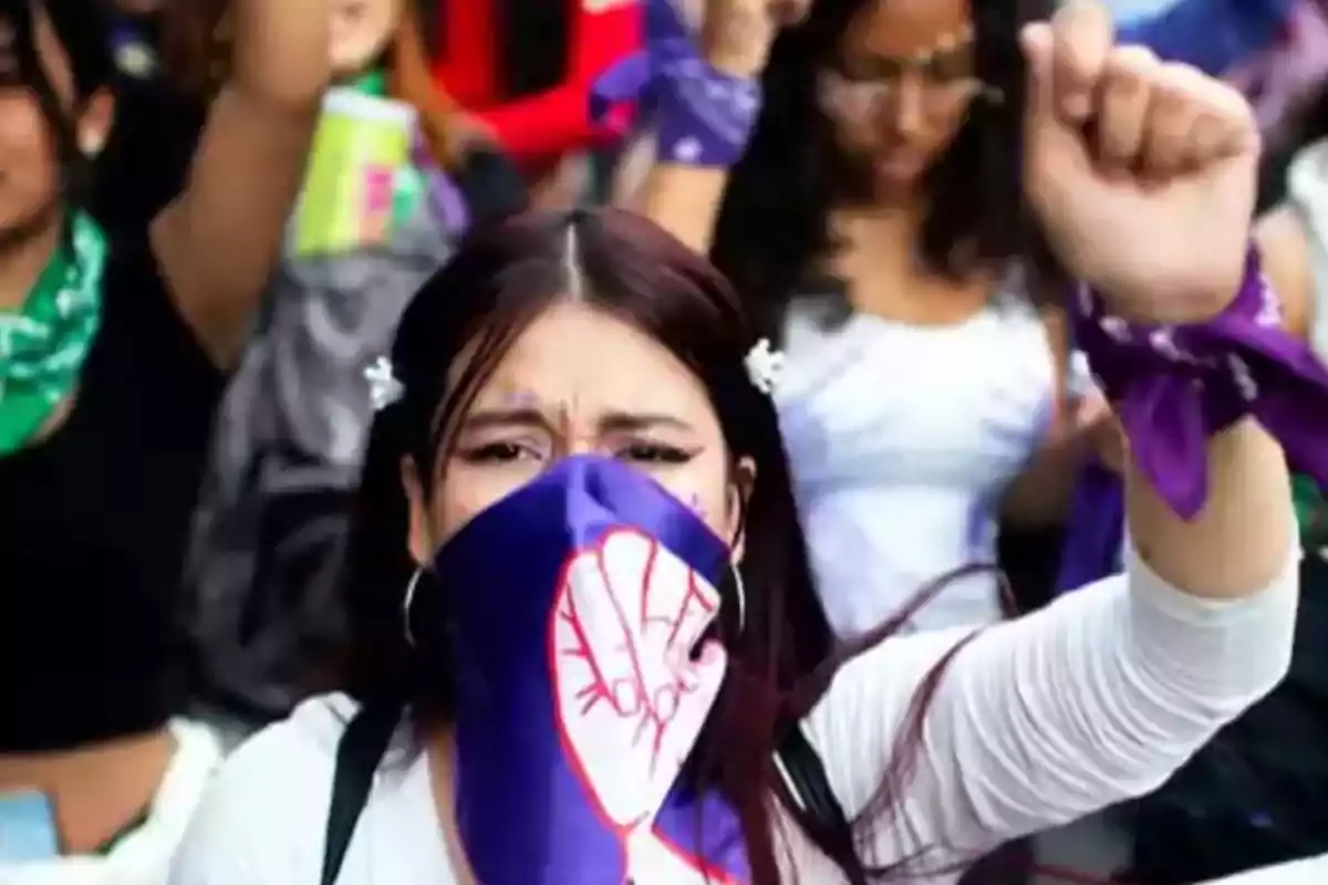 Mujer con pañuelo morado cubriéndose el rostro y levantando el puño durante una manifestación feminista