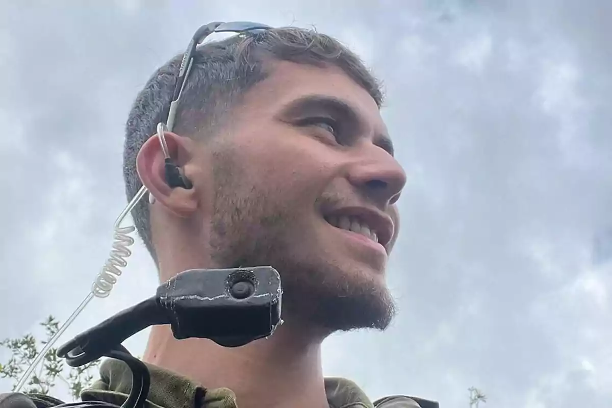 Young man with headset and microphone smiles while looking to the side under a cloudy sky