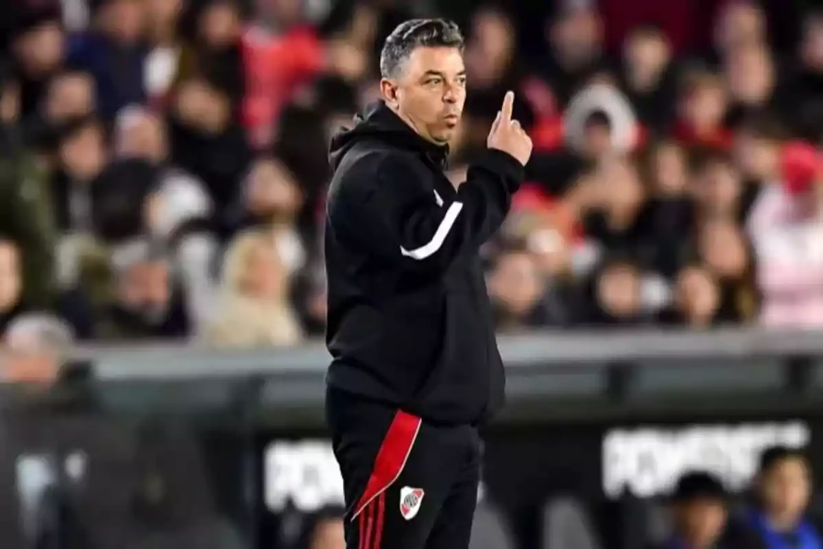 Entrenador de fútbol con ropa deportiva negra haciendo una señal con el dedo índice levantado en un estadio lleno de espectadores Entrenador de fútbol con ropa deportiva negra haciendo una señal con el dedo índice levantado en un estadio lleno de espectadores