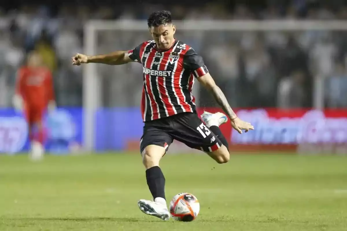 Futbolista con uniforme de rayas rojas, negras y blancas pateando un balón en un partido Futbolista con uniforme de rayas rojas, negras y blancas pateando un balón en un partido