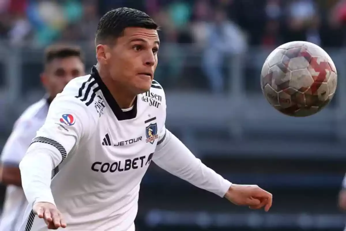 Soccer player wearing a white Colo Colo jersey closely watches a ball during the match. Soccer player wearing a white Colo Colo jersey closely watches a ball during the match.