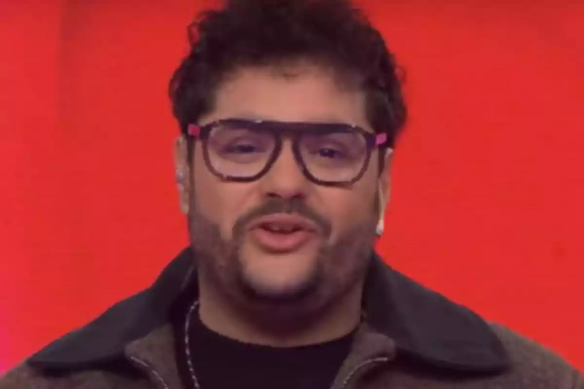 Man with large glasses and a beard in front of a red background