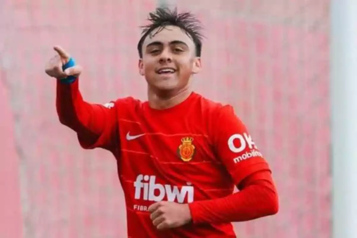 Young player in a red uniform celebrating a goal while smiling and pointing forward Young player in a red uniform celebrating a goal while smiling and pointing forward