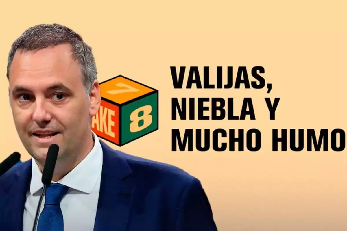 Hombre de traje y corbata hablando frente a micrófonos con un fondo beige que incluye un cubo con los números 7 y 8 y el texto Valijas niebla y mucho humo
