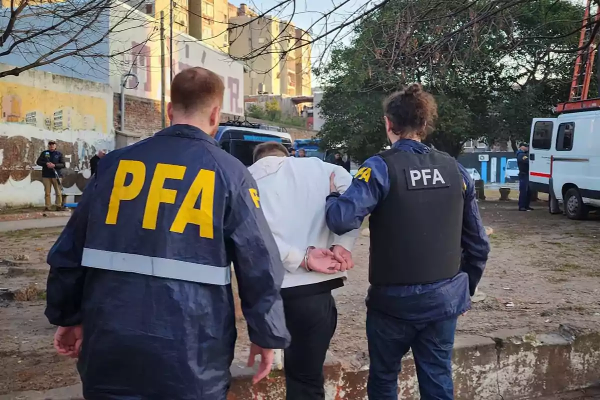 Dos agentes de la policía federal escoltan a una persona esposada en un entorno urbano Dos agentes de la policía federal escoltan a una persona esposada en un entorno urbano