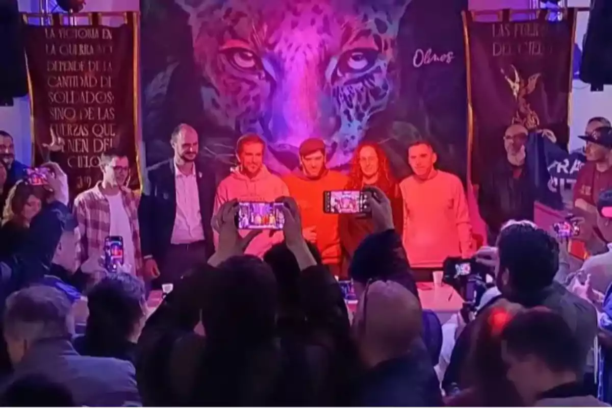 A group of people poses for a photo at an event with a backdrop of an illuminated jaguar, while several people in the audience take pictures with their phones. A group of people poses for a photo at an event with a backdrop of an illuminated jaguar, while several people in the audience take pictures with their phones.
