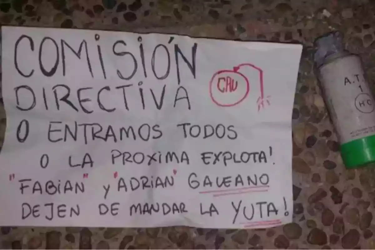 Cartel escrito a mano con un mensaje amenazante dirigido a una comisión directiva, acompañado de un objeto cilíndrico similar a un cartucho sobre el suelo. Cartel escrito a mano con un mensaje amenazante dirigido a una comisión directiva, acompañado de un objeto cilíndrico similar a un cartucho sobre el suelo.