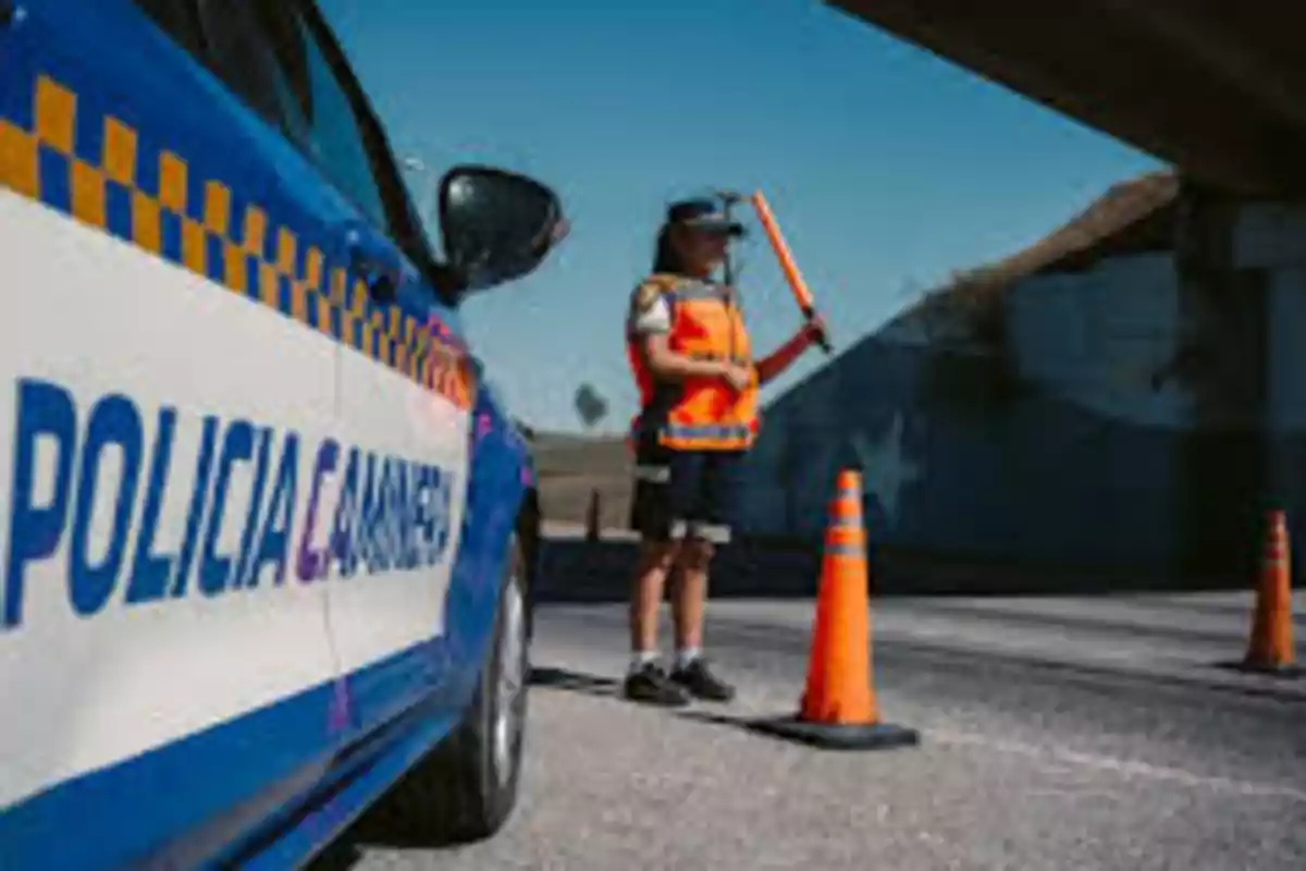 Patrulla de la policía caminera estacionada junto a un oficial que dirige el tráfico con un bastón luminoso y conos naranjas en una carretera Patrulla de la policía caminera estacionada junto a un oficial que dirige el tráfico con un bastón luminoso y conos naranjas en una carretera