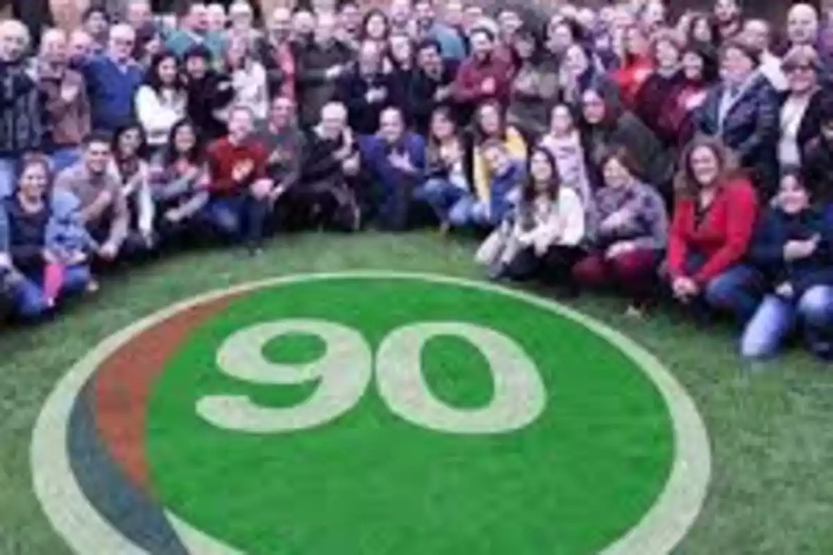 Un grupo grande de personas reunidas alrededor de un círculo verde en el césped con el número 90 en el centro Un grupo grande de personas reunidas alrededor de un círculo verde en el césped con el número 90 en el centro