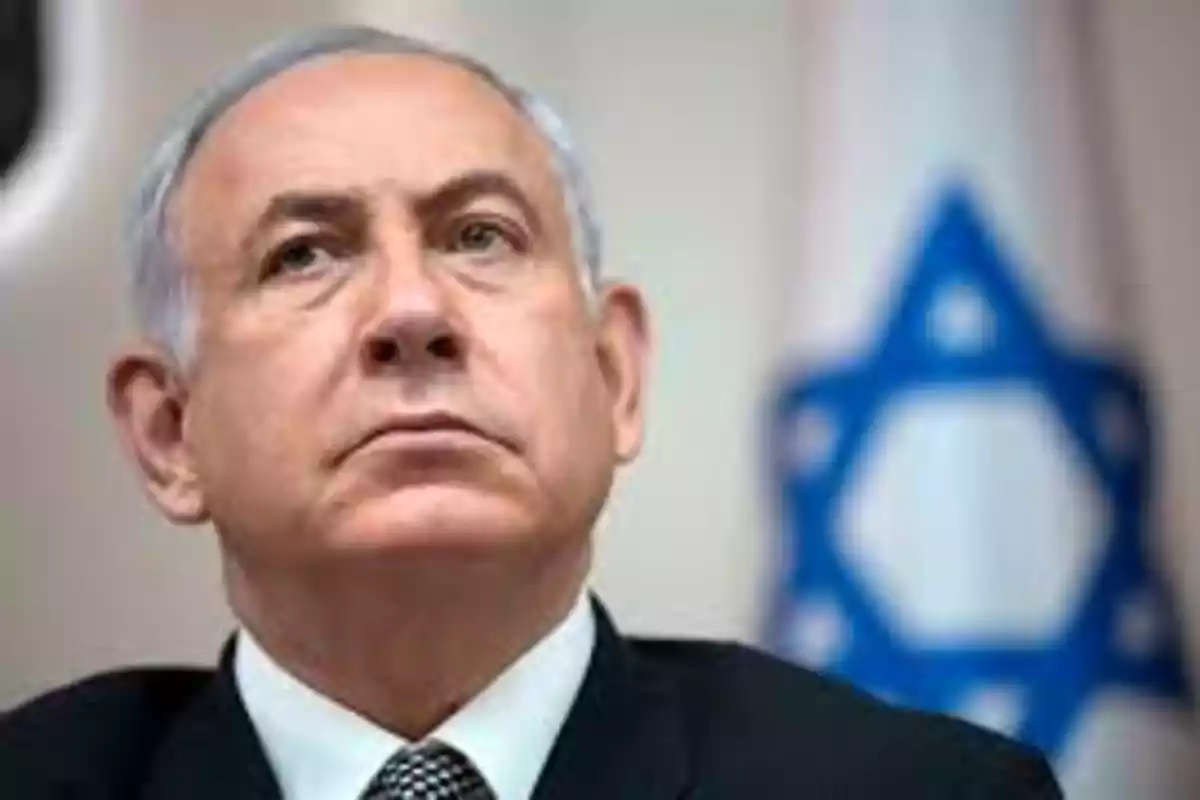 Hombre de cabello canoso con traje oscuro y corbata, al fondo una bandera con la estrella de David desenfocada Hombre de cabello canoso con traje oscuro y corbata, al fondo una bandera con la estrella de David desenfocada