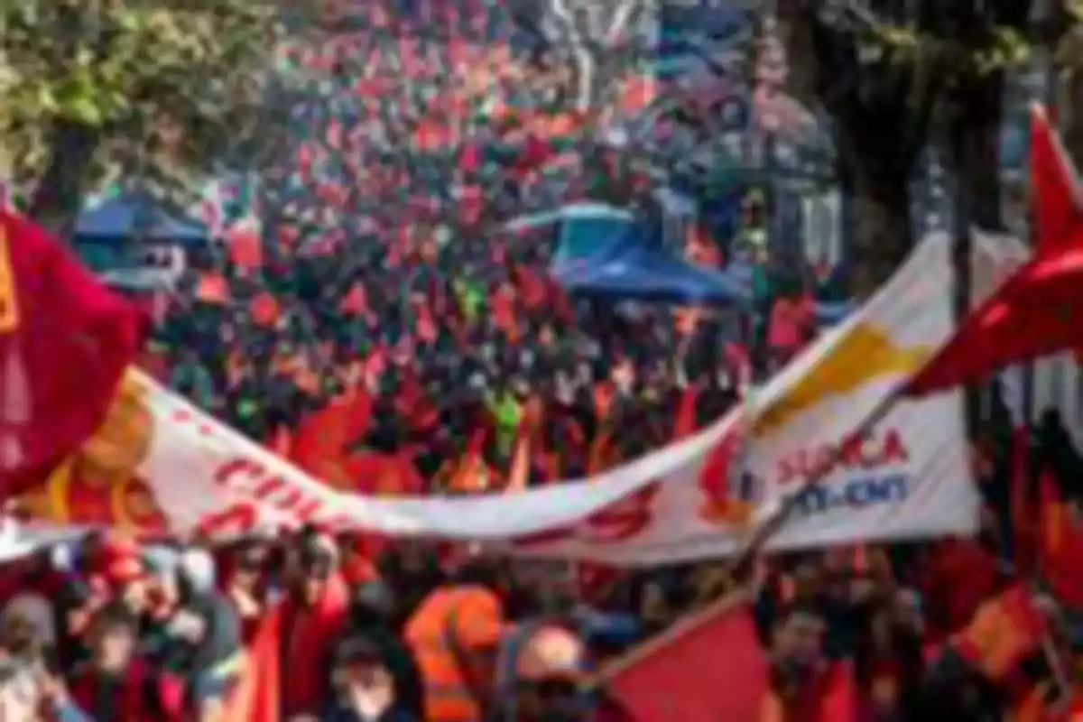 Multitud de personas marchando por la calle con banderas y pancartas rojas Multitud de personas marchando por la calle con banderas y pancartas rojas