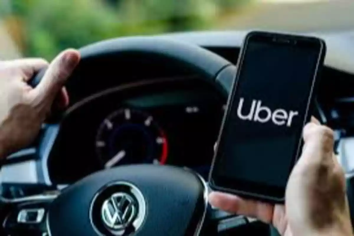 Persona conduciendo un auto Volkswagen mientras sostiene un teléfono móvil con la aplicación de Uber abierta