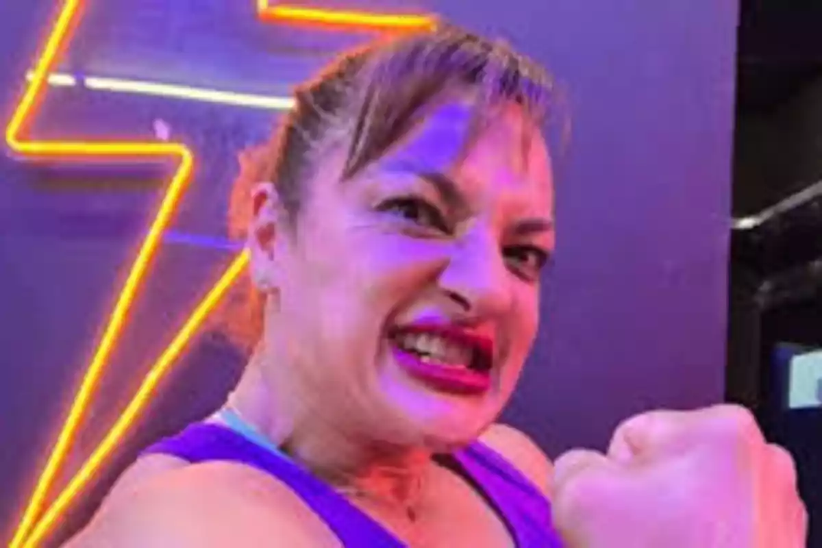 Mujer con expresión de enojo levantando el puño frente a un fondo con luces de neón en forma de rayo Mujer con expresión de enojo levantando el puño frente a un fondo con luces de neón en forma de rayo