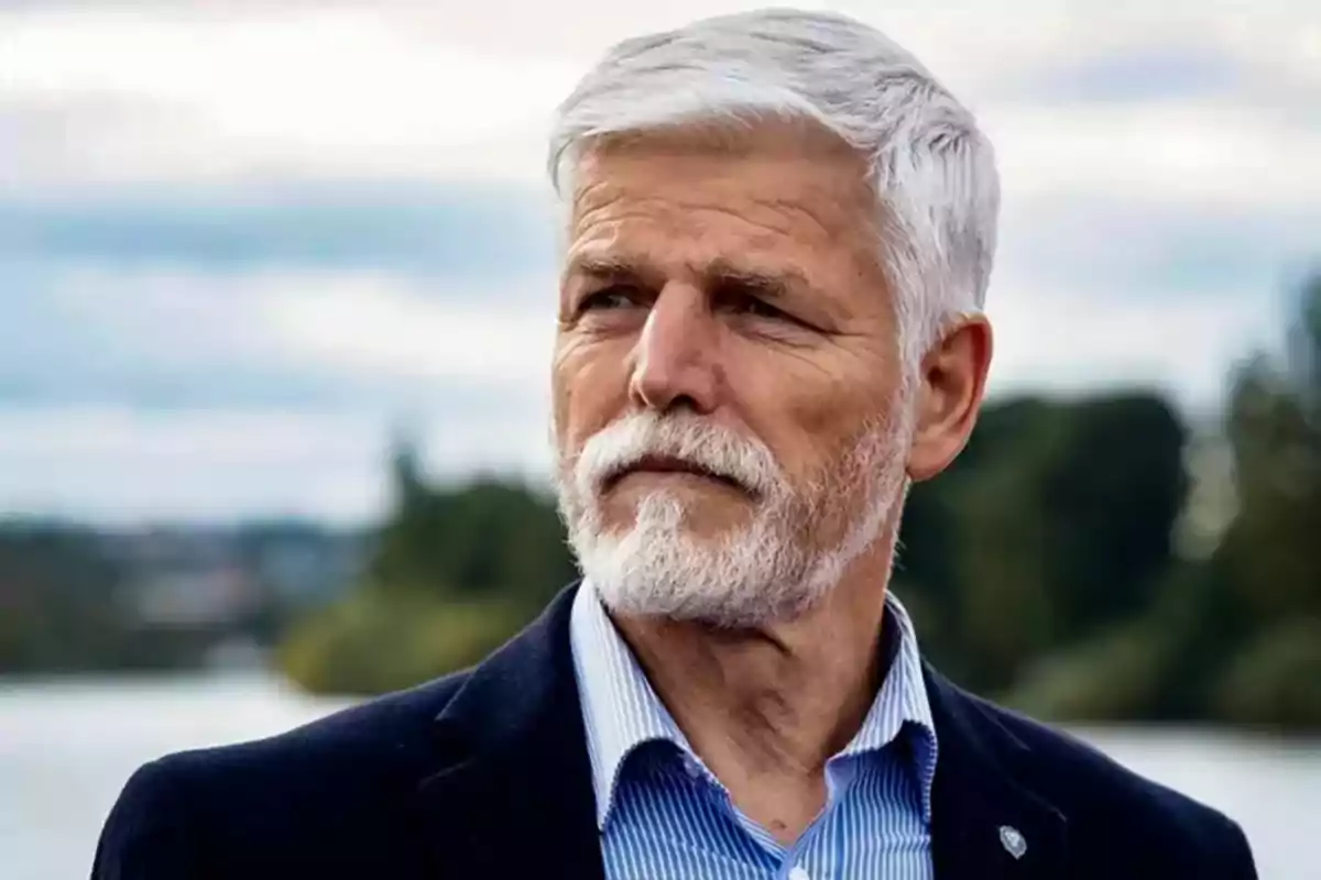 Older man with gray hair and beard, serious expression, wearing a blue jacket and striped jersey, outdoors with a blurred natural background. Older man with gray hair and beard, serious expression, wearing a blue jacket and striped jersey, outdoors with a blurred natural background.