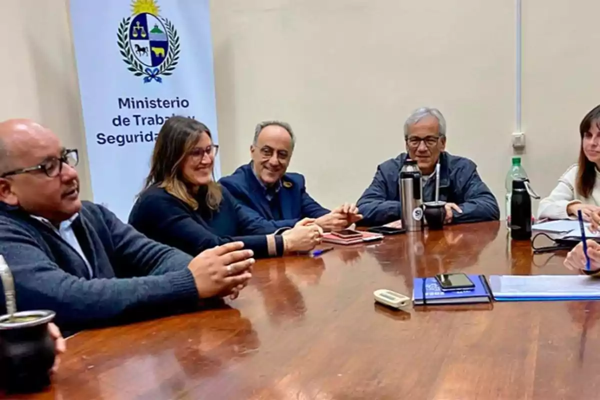 Varias personas sentadas alrededor de una mesa de madera en una reunión en una oficina del Ministerio de Trabajo y Seguridad Social Varias personas sentadas alrededor de una mesa de madera en una reunión en una oficina del Ministerio de Trabajo y Seguridad Social