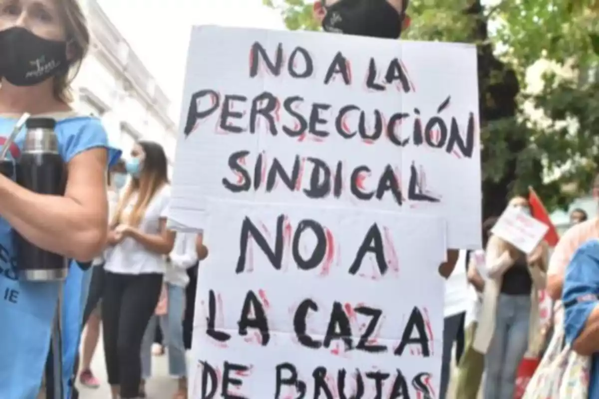 Persona sosteniendo un cartel en una manifestación que dice no a la persecución sindical no a la caza de brujas rodeada de otras personas con barbijos Persona sosteniendo un cartel en una manifestación que dice no a la persecución sindical no a la caza de brujas rodeada de otras personas con barbijos