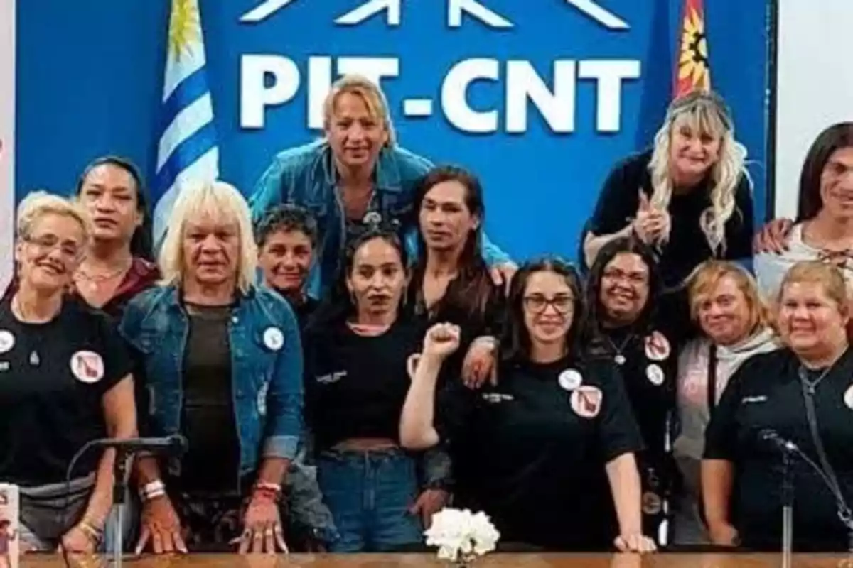 Grupo de personas posando juntas frente a un cartel azul con el texto PIT-CNT y banderas a los costados