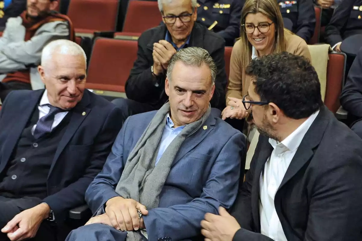 Varias personas vestidas de manera formal conversan y sonríen sentadas en un auditorio