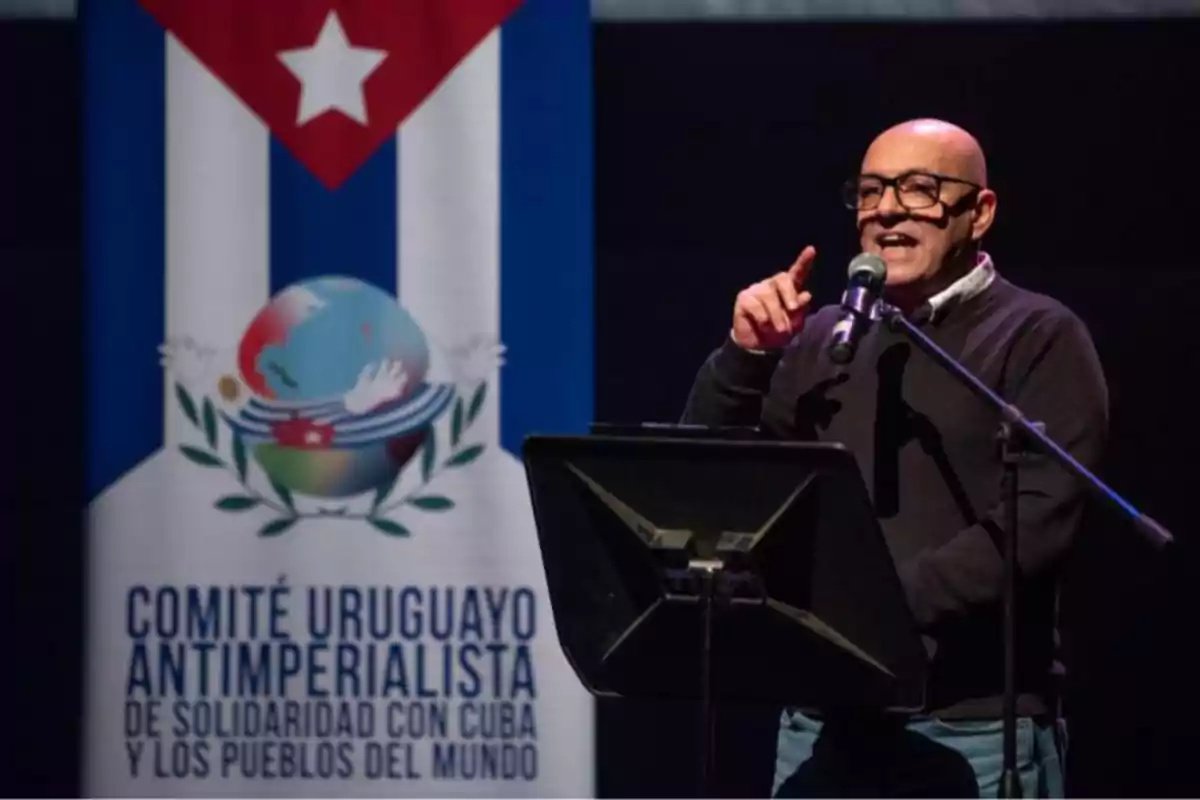 Hombre calvo con gafas hablando en un micrófono frente a un atril, junto a una pancarta del Comité Uruguayo Antimperialista de Solidaridad con Cuba y los Pueblos del Mundo Hombre calvo con gafas hablando en un micrófono frente a un atril, junto a una pancarta del Comité Uruguayo Antimperialista de Solidaridad con Cuba y los Pueblos del Mundo
