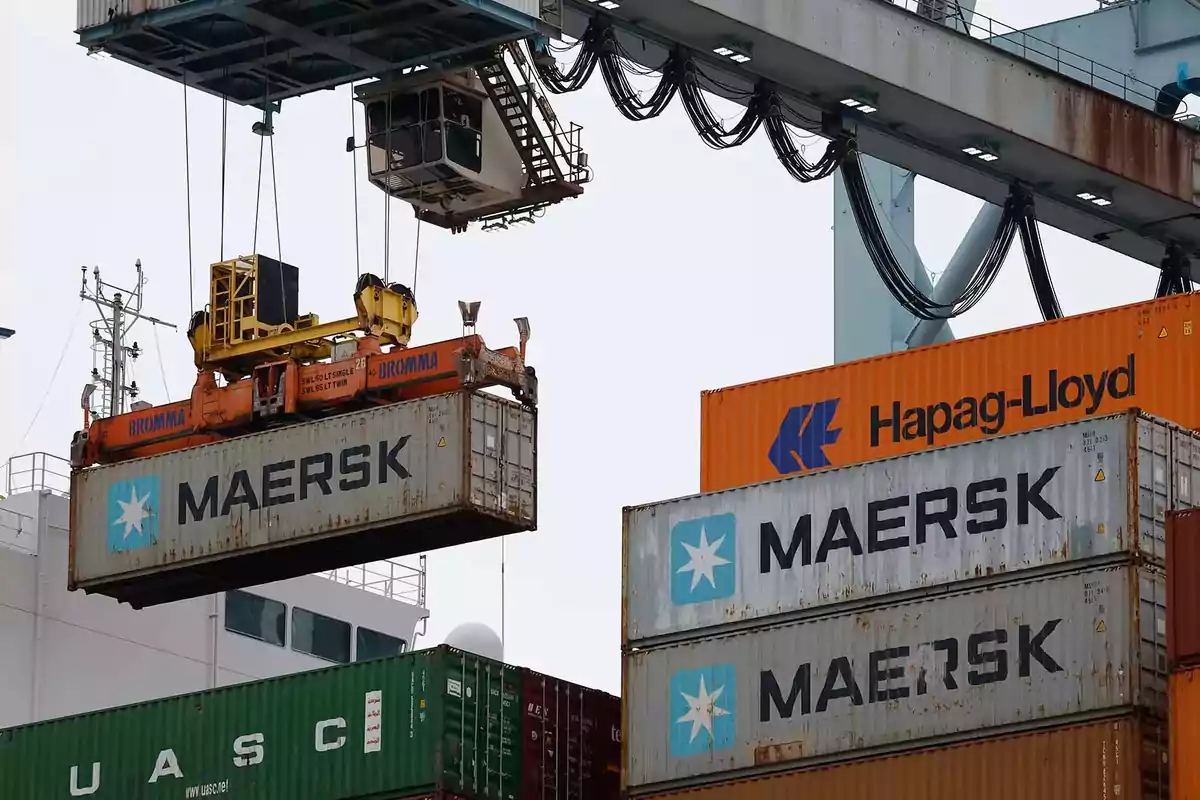 Grúa portuaria levantando un contenedor de la empresa Maersk junto a otros contenedores apilados de diferentes compañías Grúa portuaria levantando un contenedor de la empresa Maersk junto a otros contenedores apilados de diferentes compañías