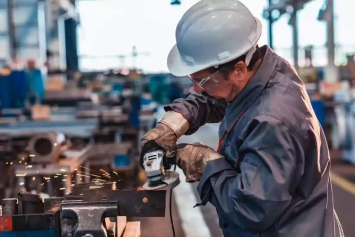 Trabajador industrial usando equipo de protección mientras utiliza una herramienta eléctrica para cortar metal en una fábrica