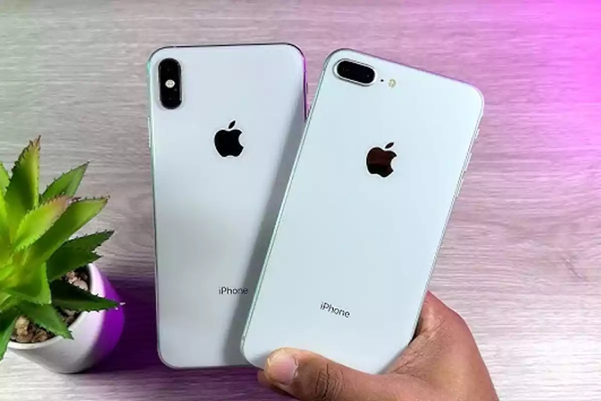 Dos iPhones plateados sobre una mesa de madera junto a una planta pequeña Dos iPhones plateados sobre una mesa de madera junto a una planta pequeña