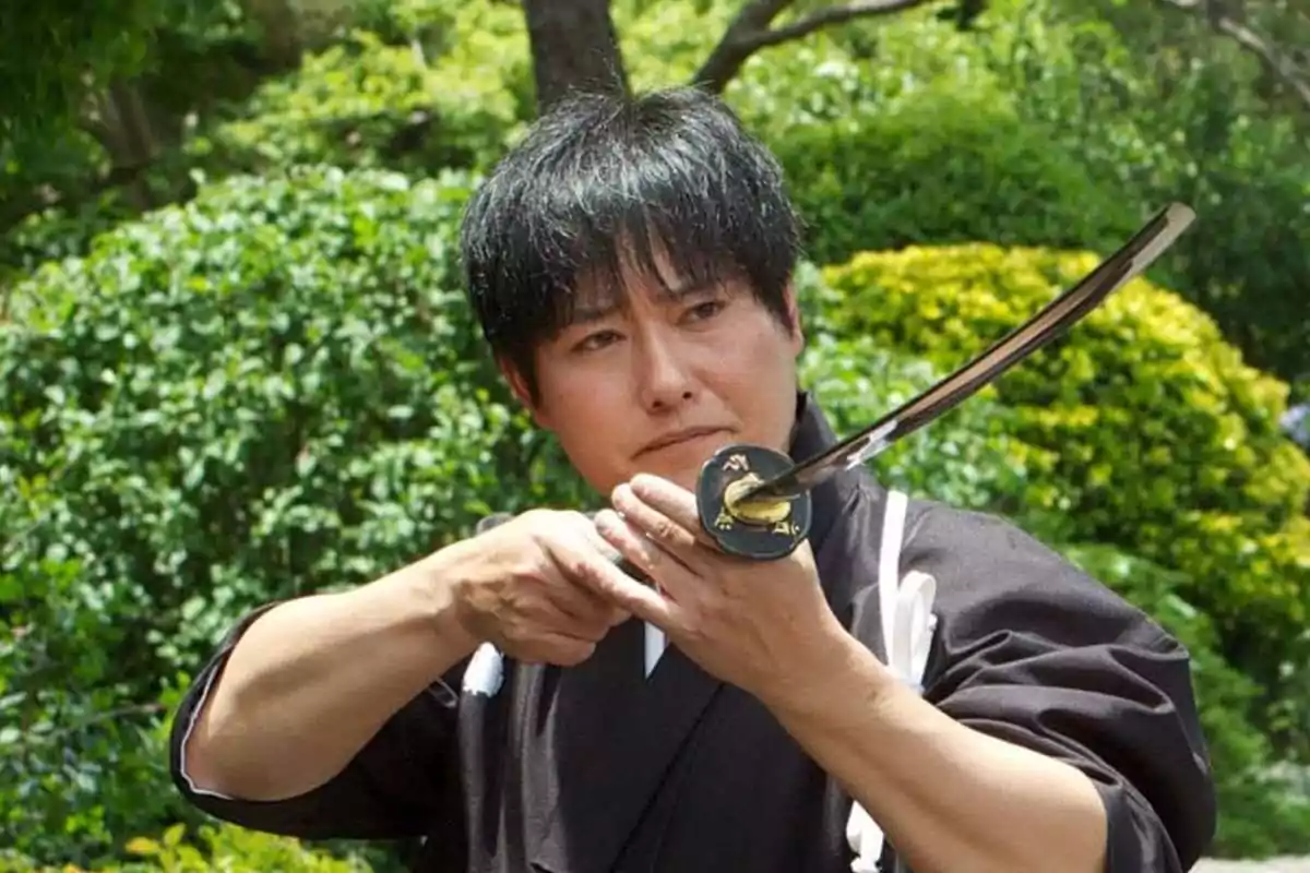 Hombre japonés sosteniendo una katana con ambas manos en un jardín verde